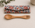 Set of floral fabric utensil case with button closure, accompanied by a wooden fork, on neutral linen background