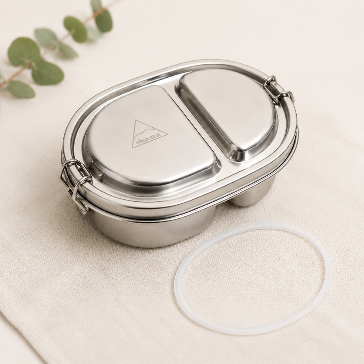 Stainless steel Shasta 500ml sealed bento box with two compartments, lid with logo, and spare seal, ideal for food storage, on beige fabric
