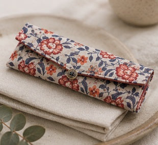 Floral fabric pouch with button closure, made of soft material, perfect for storing utensils or small accessories, on beige fabric