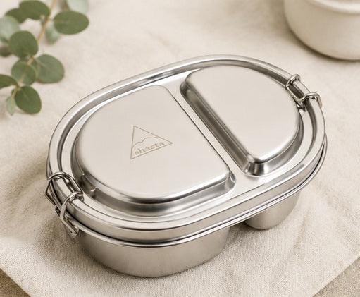 Close-up of stainless steel Shasta bento box with logo on lid, featuring two compartments and secure latch, on neutral background